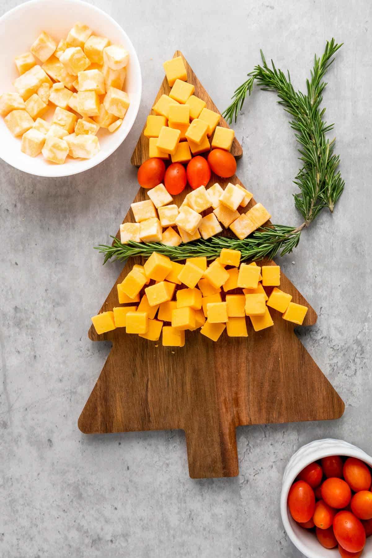 Assembling cheese on cheese board and layering tomatoes to look like Christmas tree shape.